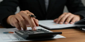 Mão segurando calculadora com documentos do INSS, simbolizando planejamento financeiro de crédito consignado em 2025.